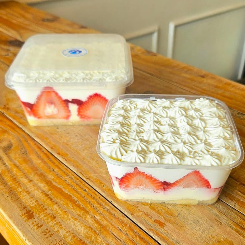 Two containers of strawberry shortcake on a wooden surface.